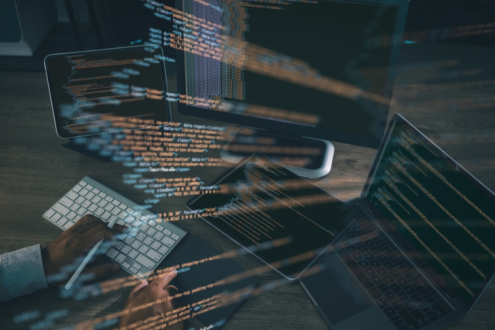 Engineer working across a laptop, tablet and monitor with code overlaid
